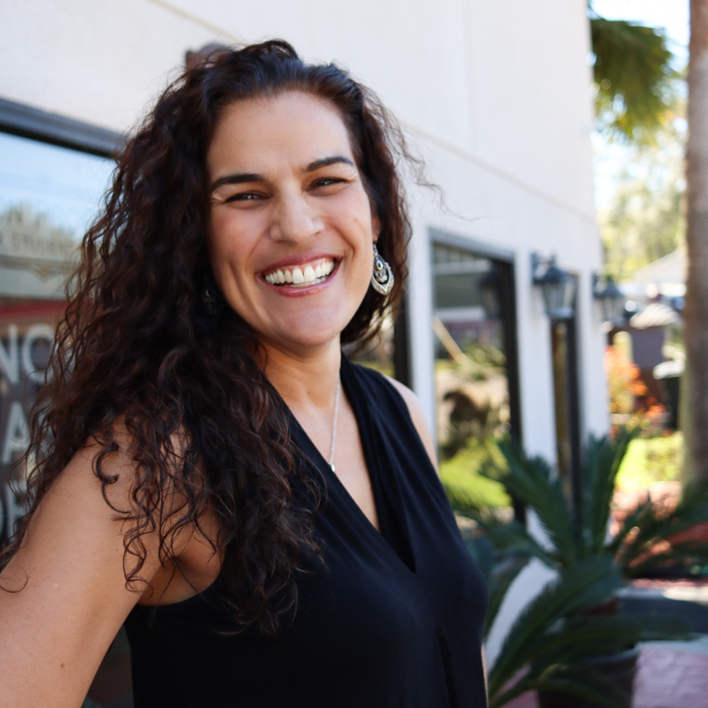 Portrait photo of Elizabeth Rosario in front of Jackson Properties in Tallahassee, Florida. She is wearing a v-neck black top and smiling at the camera. The building can be seen in the background.